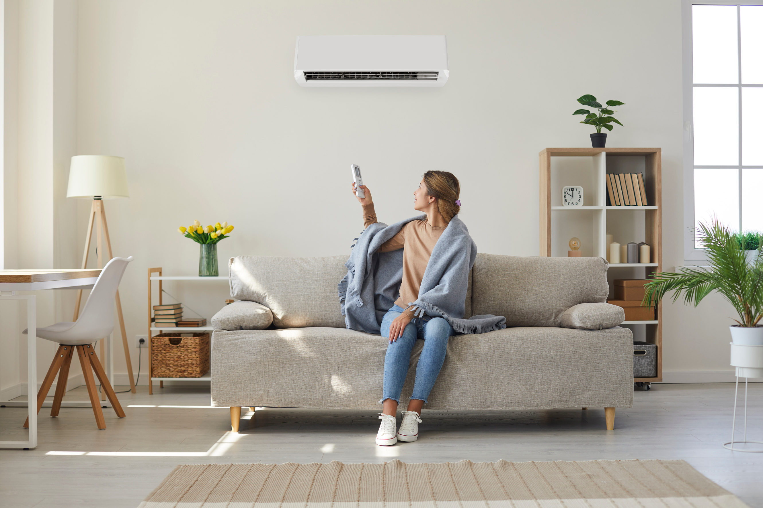 Woman enjoying cool fresh air in her living room with a ductless unit on the wall as she adjusts the temperature using a remote control.