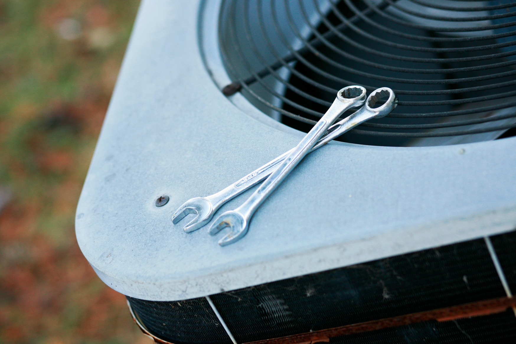 Photo of an outdoor Air conditioning unit with two wrenches on top.